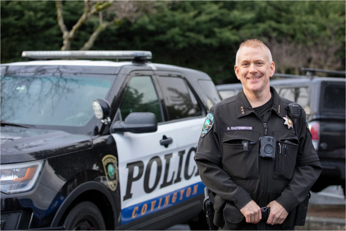 Smiling police officer in uniform standing in front of a police vehicle