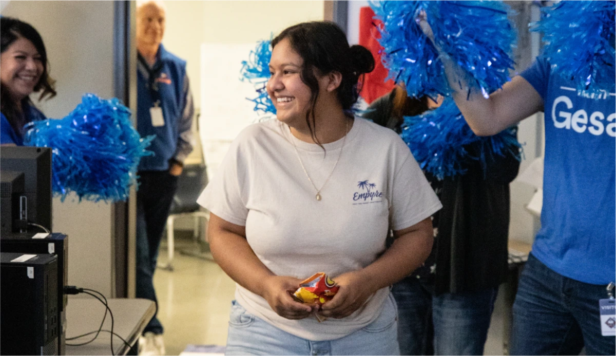 Smiling young woman in white shirt surrounded by people with blue pom-poms at an event