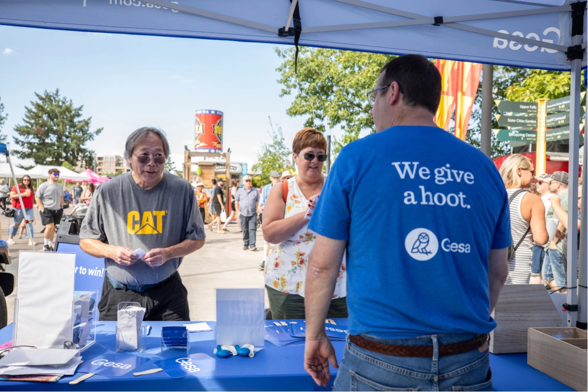 People at an outdoor booth with Gesa Credit Union branding, staff member wearing shirt that says "We give a hoot"